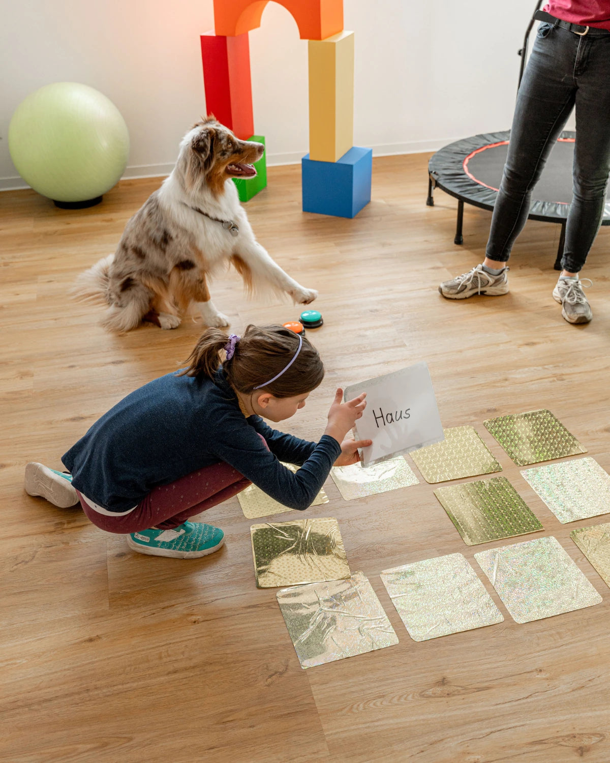 Kind bei einer therapeutischen Bewegungsübung mit Therapiehund und sensorischen Materialien in einem modernen und freundlichen Therapieraum.
